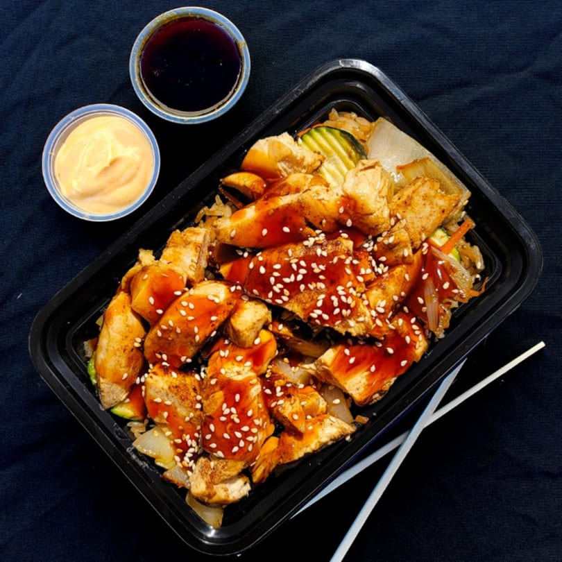 Hibachi chicken with vegetables and rice, topped with sauce and sesame seeds, with two dipping sauces.