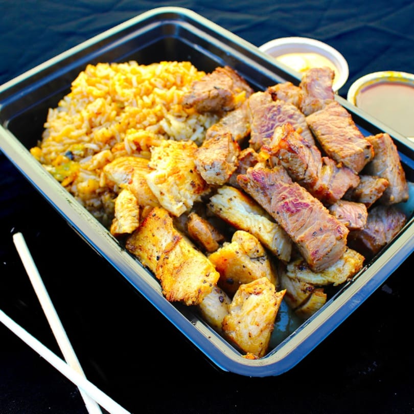 Hibachi chicken and steak with fried rice in a black takeout container, with two sauces and chopsticks.