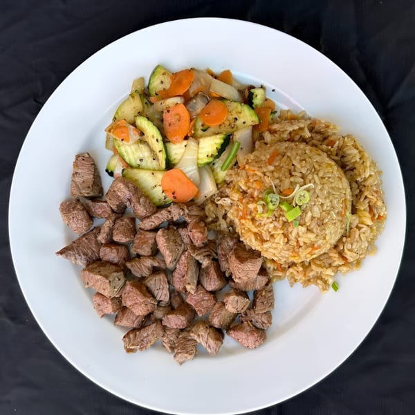 Hibachi steak, fried rice, and mixed vegetables with zucchini, carrots, and onions on a white plate.