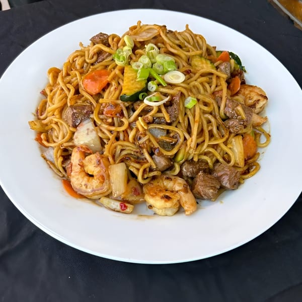Hibachi noodles with shrimp, beef, carrots, zucchini, and onions, garnished with green onions.