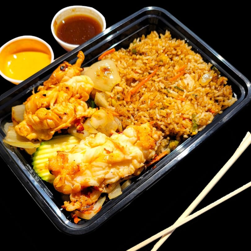 Hibachi lobster and shrimp with fried rice, vegetables, and two dipping sauces in a to-go container.